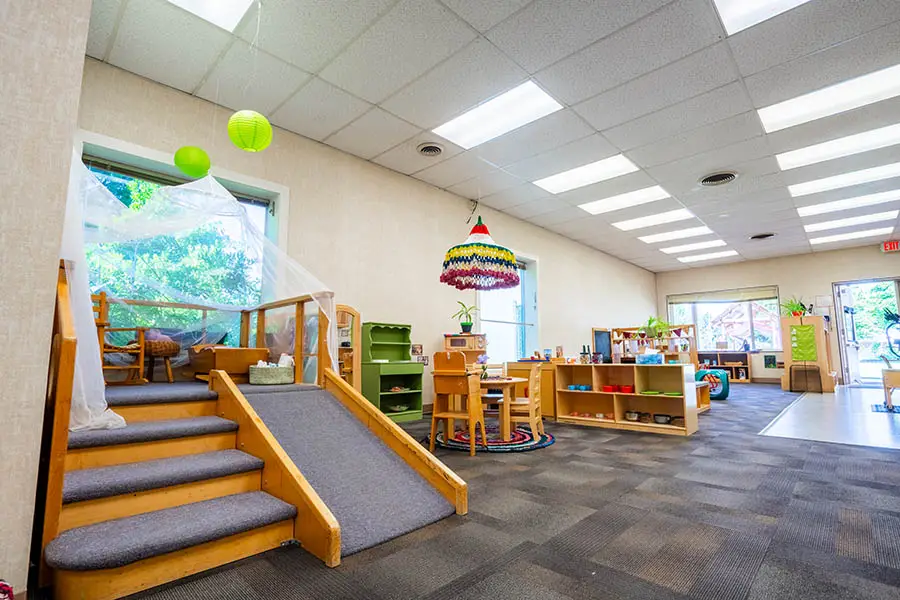 A room at Chemeketa's Child Development Center filled with children’s furniture and toys. Stairs lead up to an elevated platform with a wooden railing. The walls are white with fluorescent lighting overhead.